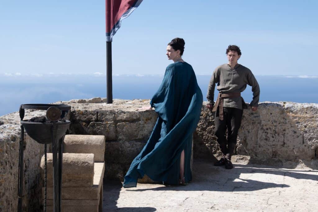 Anne Hathaway as Penelope and Tom Holland as Telemachus in The Odyssey. The mother and son duo are looking out at sea from the palace rooftop.
