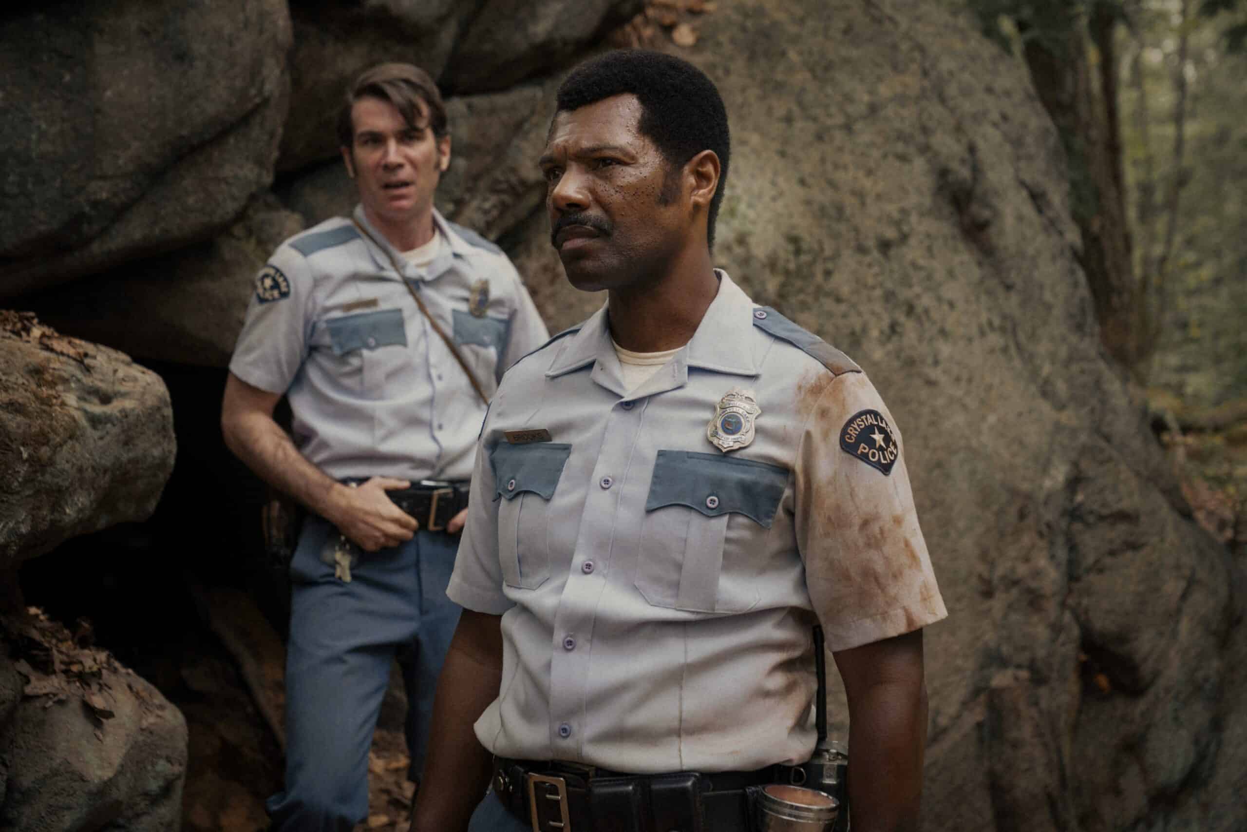 Cameron Scoggins as Dorf, William Catlett as Levon. The chief of police and his deputy are outdoors, looking out in the distance, Levon is in the foreground with a worried expression on his face.