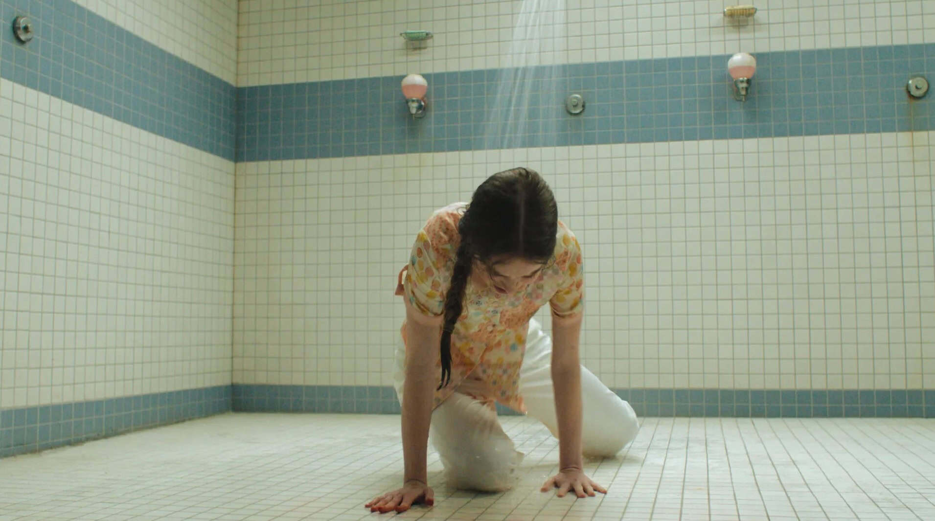 Summer H Lowell cries in the shower as Carrie. She's fully clothed and gazing down, kneeling on the floor.