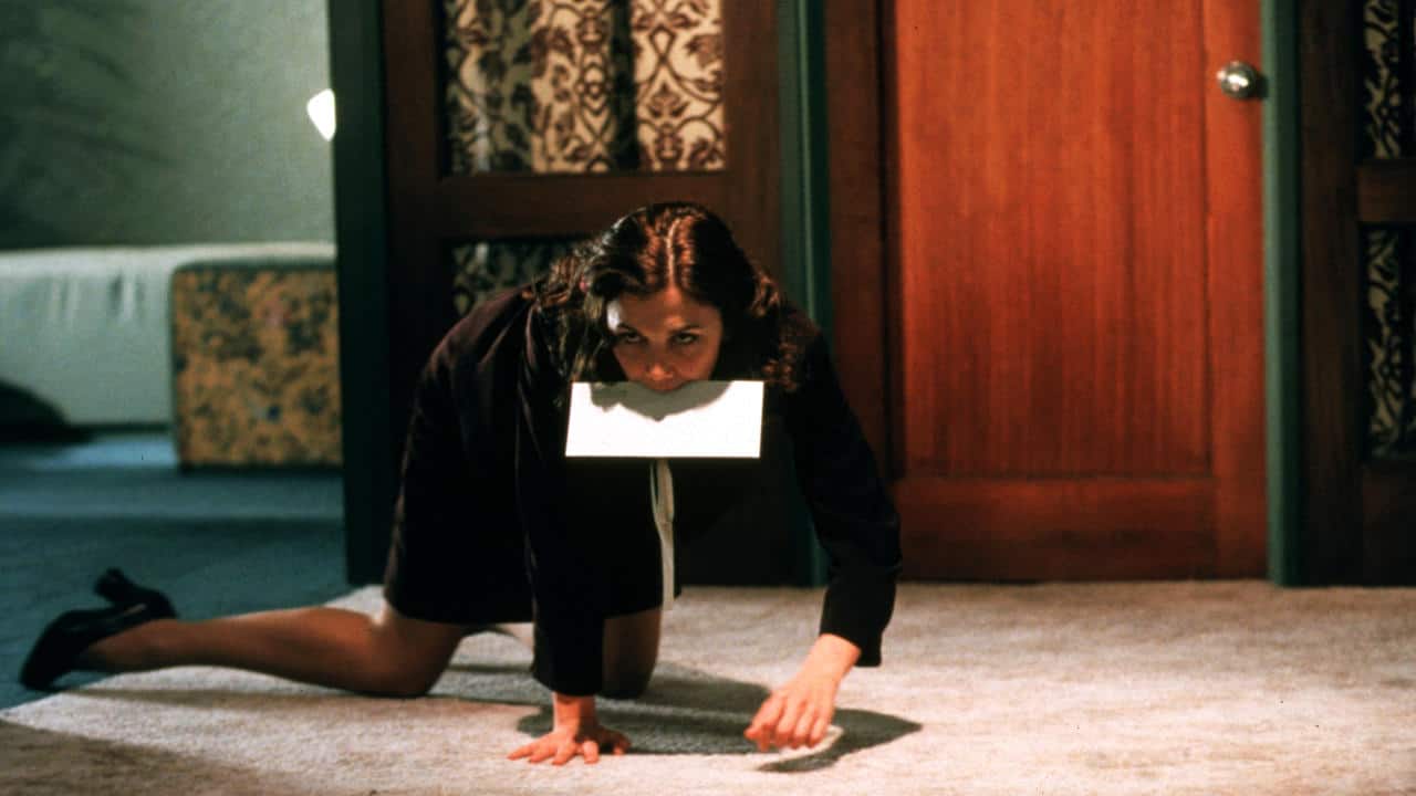 Maggie Gyllenhaal as Lee in a scene of Secretary. She is on all fours as she holds an envelope in between her teeth.